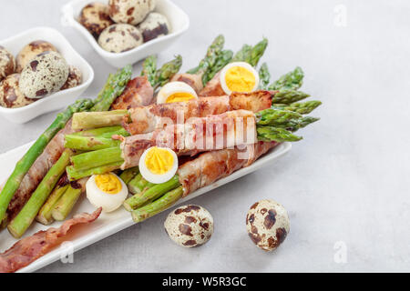 Spargel mit Speck. Grüner Spargel in Schinken mit gekochte Wachteleier gewickelt. Stockfoto