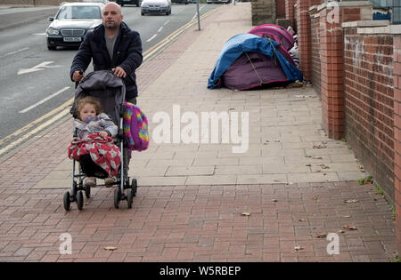 Ein Mann schiebt ein Kind im Kinderwagen Vergangenheit Obdachlosen Zelte tagsüber auf Trinity St, Bolton, North West England UK Foto DON TONGE Stockfoto