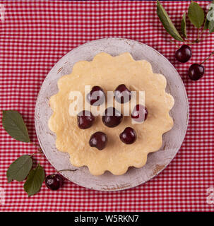 Hausgemachter Käsekuchen mit Kirschen auf weiß rot karierten Stoff Hintergrund eingerichtet. Ansicht von oben Stockfoto