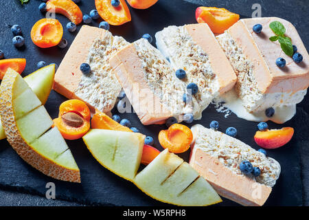 In der Nähe von Schmelz Semifreddo alle Mandorle, sizilianischen Almond apricot Melone Semifreddo auf einer Schiefertafel Teller mit Früchten und Beeren serviert, Ansicht von abov Stockfoto