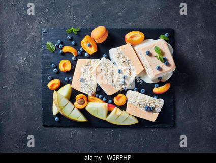 In der Nähe von Schmelz Semifreddo alle Mandorle, sizilianischen Mandeln Semifreddo mit Aprikose und Melone in Scheiben geschnitten auf einer Schiefertafel Teller mit Früchten und Beeren, Anzeigen Stockfoto