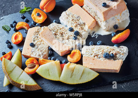 Italienischen sommers Dessert, schmelzen Semifreddo alle Mandorle, sizilianischen Almond apricot Melone Semifreddo auf einer Schiefertafel Teller mit Früchten und Beeren serviert, Ho Stockfoto