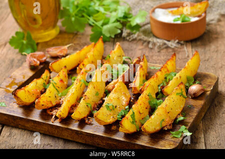 Frittierte Kartoffelecken mit Gewürzen und Kräutern auf Schneidebrett Stockfoto