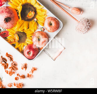 Fach mit Äpfeln, Sonnenblumen und Granatapfel auf weißen Tisch mit Herbstlaub und botanischen Dekoration, Ansicht von oben. Flach. Modern. Minimal. Fallen se Stockfoto