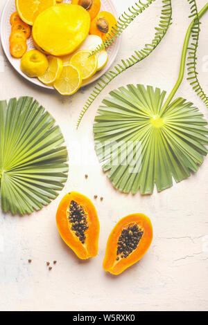 Halbiert reife Papaya Früchte mit Samen auf weißen Tisch mit tropischen Blättern und Schild mit gelbem geschnittenes Obst, Ansicht von oben. Im Sommer essen. Das gesunde Essen. Br Stockfoto