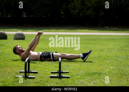 Mann, Aufwärmen, bevor Sie calisthenics Fitness Training in einen öffentlichen Park, Großbritannien Stockfoto