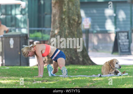 25.07.2019. Battersea, London, UK. Eine Frau erstreckt sich auf das Gras selbst Schattierung von der Mittagssonne in Battersea Park als eine Hitzewelle über Th fegt Stockfoto