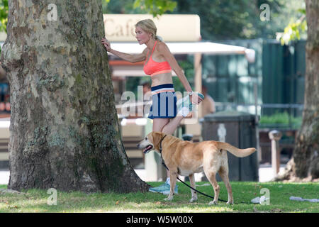 25.07.2019. Battersea, London, UK. Eine Frau erstreckt sich auf das Gras selbst Schattierung von der Mittagssonne in Battersea Park als eine Hitzewelle über Th fegt Stockfoto