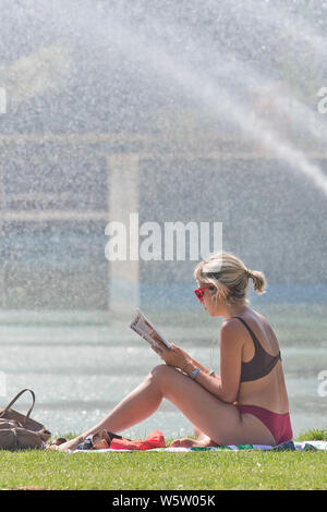 25.07.2019. Battersea, London, UK. Eine Frau liest vom Brunnen in der Mittagshitze in Battersea Park als eine Hitzewelle fegt über Großbritannien. Stockfoto