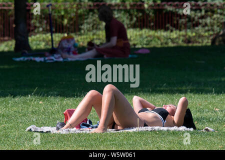 25.07.2019. Battersea, London, UK. Eine Frau auf dem Gras sunbathes in Battersea Park als eine Hitzewelle fegt über Großbritannien. Stockfoto