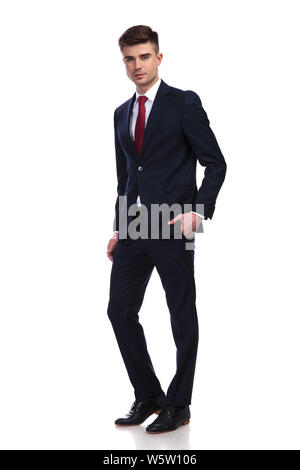 Zuversichtlich, dass junge Unternehmer tragen eine Marine Anzug und eine rote Krawatte, stehend und mit der Hand in der Tasche posiert auf weißem Hintergrund, Bild Stockfoto