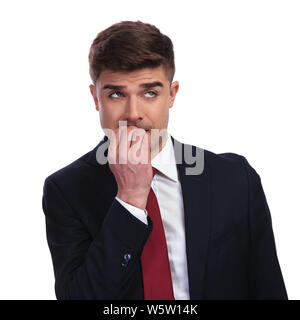 Portrait von betonte Geschäftsmann seine Nägel beißen und bis auf die Seite beim Stehen auf weißen Hintergrund. Er trägt eine marine farbigen Anzug und einem roten t Stockfoto