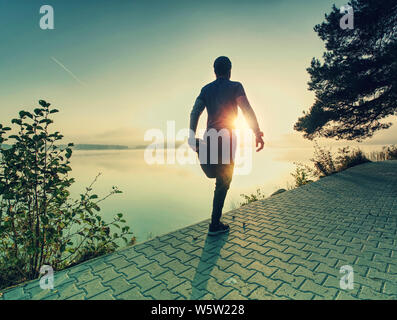 Athlet stretching untere Körper Kniesehne Muskeln, bevor Sie laufen am See im Sommer im Freien. Stockfoto