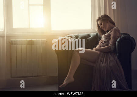 Schöne schwangere Frau auf dem Sofa zu Hause sitzen Stockfoto