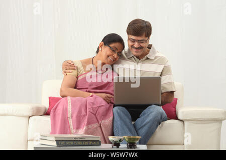 Ein älterer Mann, der mit seiner Frau einen Laptop benutzt und lächelt Stockfoto