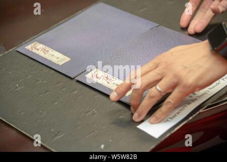 Ein Mitarbeiter zeigt die Handschriften der Sondermarken zum Thema "Zeichen in Jin Yongs Romane in einer Filiale von Hongkong Post in Hongkong, China, Stockfoto