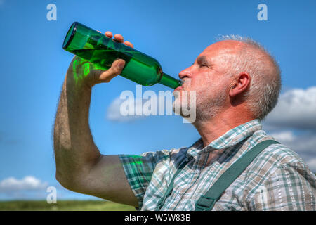 Ein Landwirt bei der Ernte Getränke sauberes Wasser aus seiner Trinkflasche in der Hitze der Mittagssonne. Stockfoto