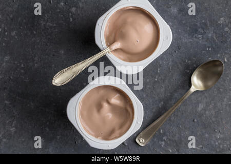 Zwei Schokolade aromatisierten Joghurt in Plastik Becher mit Löffeln auf grau Textur Hintergrund - Ansicht von oben Foto von joghurtbecher Stockfoto