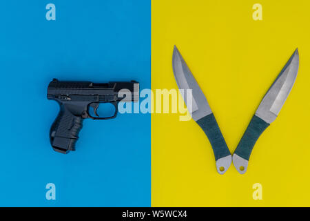 Schwarze Pistole und zwei wurfmesser auf einem farbigen Hintergrund. Blauen und gelben Hintergrund. Stockfoto