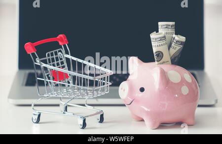 Warenkorb und Sparschwein mit Laptop auf dem Schreibtisch, Online Shopping Konzept Stockfoto