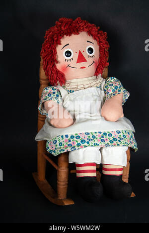 Old rag doll mit weißen Schürze in einem hölzernen Schaukelstuhl sitzen Stockfoto