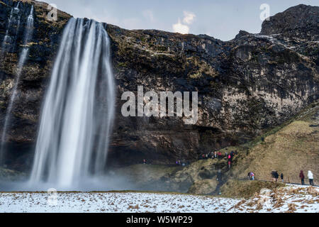 Touristen, kaltes Wasser Brise aus Seljalandsfos Wasserfall im Winter in Island Stockfoto