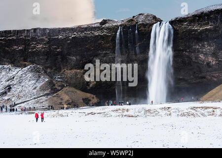 Touristen, kaltes Wasser Brise aus Seljalandsfos Wasserfall im Winter in Island Stockfoto