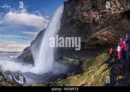 Touristen, kaltes Wasser Brise aus Seljalandsfos Wasserfall im Winter in Island Stockfoto