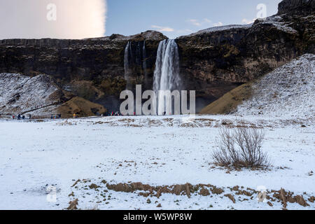 Touristen, kaltes Wasser Brise aus Seljalandsfos Wasserfall im Winter in Island Stockfoto