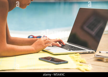 Nahaufnahme eines Jungen mit Laptop in der Nähe der Pool in einem sonnigen Tag. Nahaufnahme der junge Hände schreiben auf einer PC-Tastatur. Arbeiten in einem vacatio Stockfoto