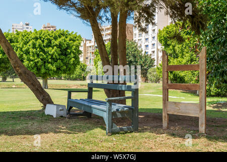 Grün leer Holzbank im Schatten von Bäumen im städtischen Park auf sonnigen Sommertag Stockfoto
