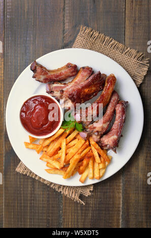 Gebratene Rippchen, Kartoffel, Pommes und Tomatensauce auf weiße Platte, Ansicht von oben Stockfoto