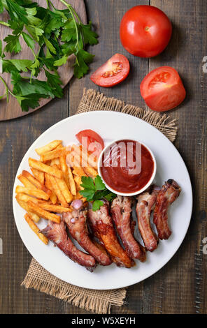 Gegrillte Schweinerippchen, Gemüse, Kartoffel, Pommes und Tomatensauce auf Holztisch, Ansicht von oben Stockfoto