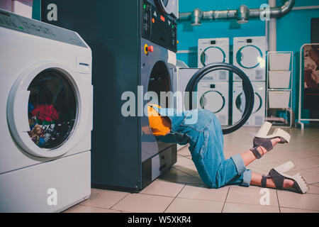 Junge Frau suche Kleidung in Waschmaschine Waschautomat drum. Stockfoto