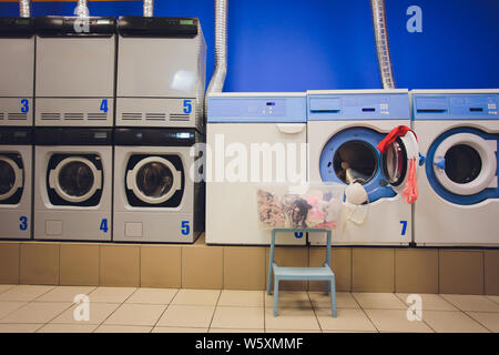 Professionelle Waschmaschinen mit Körben voller Kleider an den SB-Waschsalon. Stockfoto