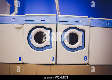 Professionelle Waschmaschinen mit Körben voller Kleider an den SB-Waschsalon. Stockfoto