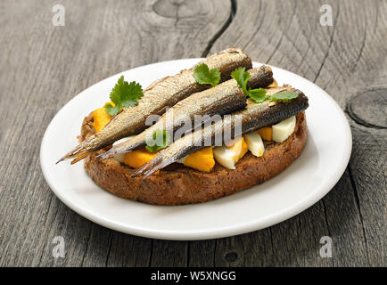 Sandwich mit Sprotten und Ei auf Holztisch, Nahaufnahme Stockfoto