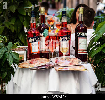 Flaschen Campri und Aperol auf einem Tisch zusammen Pizza und Menüs außerhalb ein Cafe in Rom, Italien Stockfoto