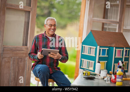 Lächelnd älterer Mann hält ein iPad, während in einer Garage, die an einem Puppenhaus. Stockfoto