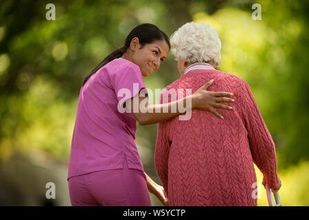 Glückliche junge Krankenschwester hilfreich unterstützen eine ältere Patienten außerhalb zu gehen. Stockfoto
