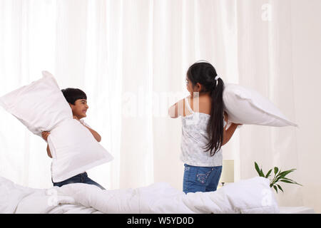 Bruder und Schwester kämpfen mit Kissen auf dem Bett Stockfoto