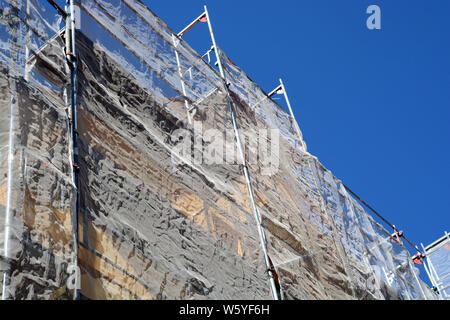Schutzgitter und Gerüsten bedeckt altes Haus Fassade während der Sanierung vor dem azurblauen Himmel, Gerüste und schützen die Verrechnung auf Hausfassade Stockfoto