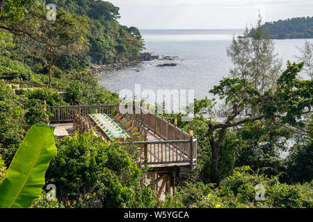 Holz- Stühle und Tische zum Mittag- und Abendessen auf der Terrasse im Freien neben Wald und Meer. Stockfoto