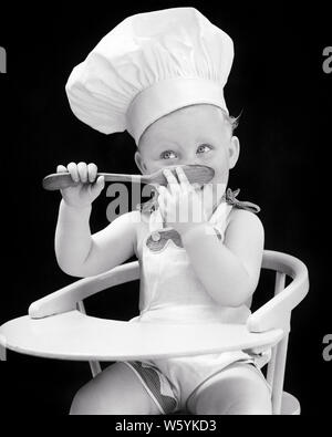 1940 s Baby Mädchen sitzen IN EINEM HOCHSTUHL TRÄGT KOCH HAT TASTING von HOLZLÖFFEL-b 13089 HAR 001 HARS B&W KLEINKINDER VERSUCHUNG GLÜCKS GESCHMACK VERKOSTUNG SPIELEN ANZUG YUMMY HOCHSTUHL JUGENDLICHE TOQUE BABY GIRL SCHWARZ UND WEISS KAUKASISCHEN ETHNIE KÜCHENCHEF DES HAR 001 ALTMODISCH Stockfoto