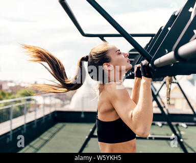 Weibliche Athleten trainieren chin-ups. Seitenansicht der jungen Frau zu tun Training auf einer Dachterrasse. Stockfoto