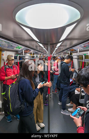 Passagiere auf eine MTR U-Bahn, die alle einen Blick auf ihre Smartphones, Hongkong, China Stockfoto