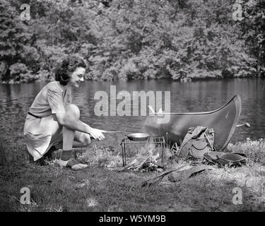 1940er lächelnd unabhängige junge Frau auf KANUTOUR VORBEREITEN MAHLZEIT ÜBER OFFENEM LAGERFEUER NEBEN STREAM-c 2336 HAR 001 HARS IN VOLLER LÄNGE MALERISCHE INSPIRATION STREAM RISIKO SPIRITUALITÄT VERTRAUEN TRANSPORT AUSDRÜCKE B&W FREIHEIT ERFOLG ZEIT KANU TRÄUME GLÜCK FRÖHLICHEN ABENTEUER DISCOVERY FREIZEITAKTIVITÄTEN STÄRKE REISE KURZURLAUB ERFAHRENE WAHL ERHOLUNG UNABHÄNGIGE STOLZ AN FEIERTAGEN LÄCHELT KONZEPTIONELLE NEBEN ESCAPE FREUDIGE STILVOLLE ENTSPANNUNG ZWEIFARBIGE SCHUHE FERIEN junger Erwachsener FRAU SCHWARZ UND WEISS IN KAUKASISCHEN ETHNIE HAR 001 ALTMODISCH Stockfoto