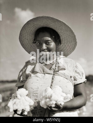 1930er lächelnd afrikanische amerikanische junge Frau mit STROHHUT AUF KAMERA HALTEN ZWEI HANDVOLL GEPFLÜCKT BAUMWOLLE LOUISIANA USA-c 6358 HAR 001 HARS FRAUEN JOBS LÄNDLICHEN HALBE LÄNGE DAMEN PERSONEN BERUF VERTRAUEN LANDWIRTSCHAFT B&W AUGENKONTAKT SKILL TRÄUME BERUF GLÜCK FÄHIGKEITEN FRÖHLICHE KRAFT afrikanischer Amerikaner MUT afrikanisch-amerikanische KARRIERE SCHWARZ ETHNIZITÄT ARBEIT LOUISIANA STOLZ IN DER BERUFE ABGEHOLT LÄCHELT KONZEPTIONELLE STROHHUT FREUDIGE STILVOLLE TEILPÄCHTER junger Erwachsener FRAU SCHWARZ UND WEISS HAR 001 LA ALTMODISCHE afrikanische Amerikaner Stockfoto