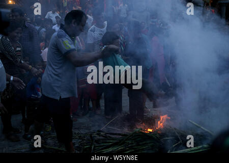 Ein Mann schwingt ein Kind um ein brennendes Feuer aus einem Bildnis des Daemon Ghantakarna die Zerstörung des Bösen während des Gathamuga oder Ghantakarna Festival zu symbolisieren. Nepalesische glauben, dass das Festival wehrt böse Geister und bringt Frieden und Wohlstand. Stockfoto