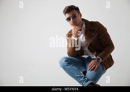 Cool junge Mode Mann hält Kinn beim Sitzen auf einem Stuhl im Studio Stockfoto